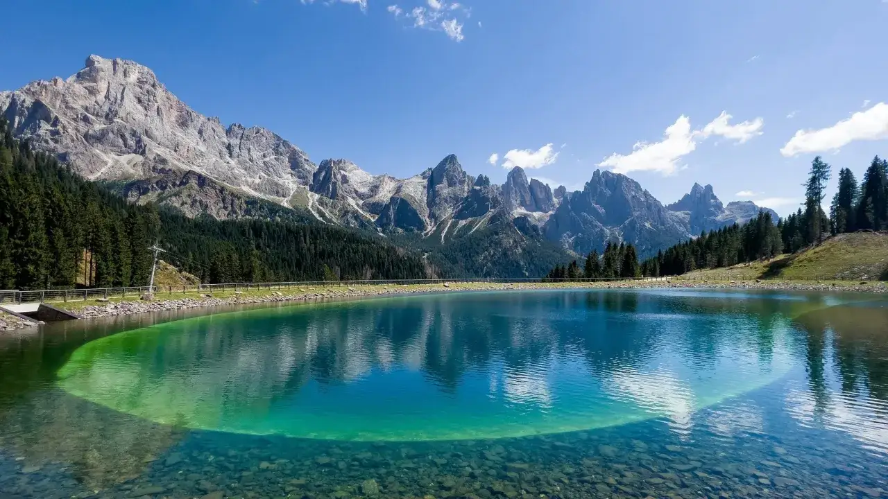 Lago alpino cristallino con montagne maestose e foreste verdi, un gioiello tra le valli del Trentino pi&ugrave; belle.
