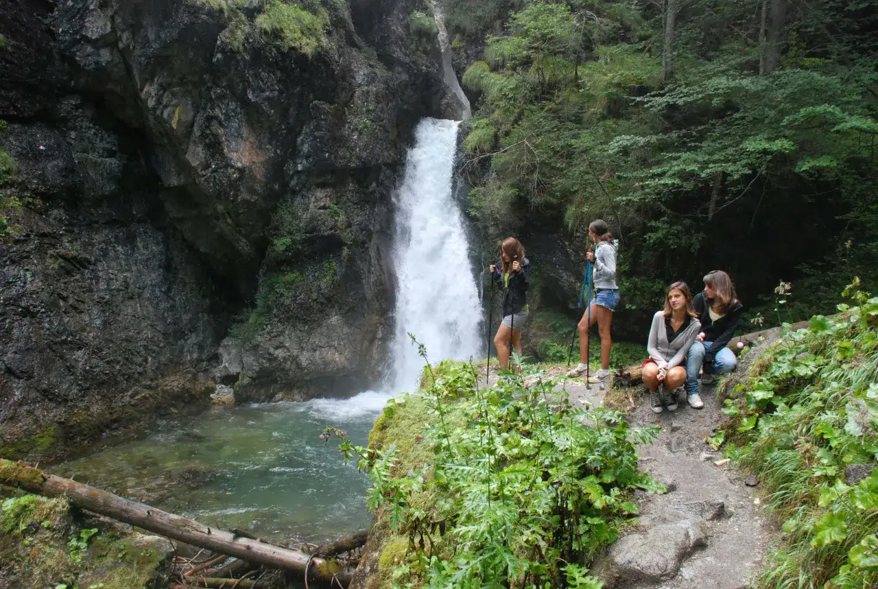 Quattro ragazze ammirano le spettacolari cascate Val di Sole, immerse nel verde della natura.