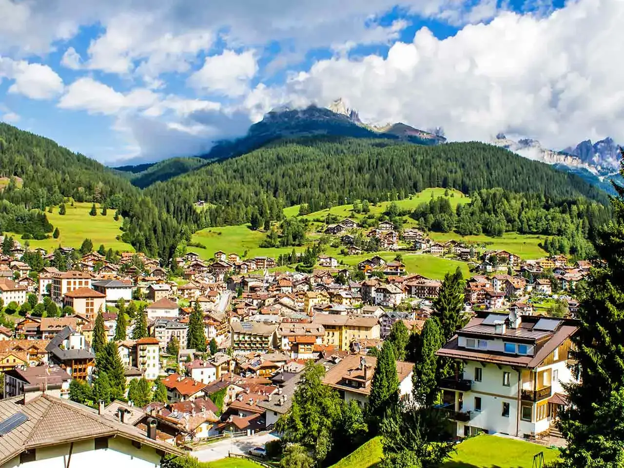 Un villaggio alpino nel Trentino, ideale per un camper tour. Case con tetti spioventi tra boschi verdi e montagne maestose.