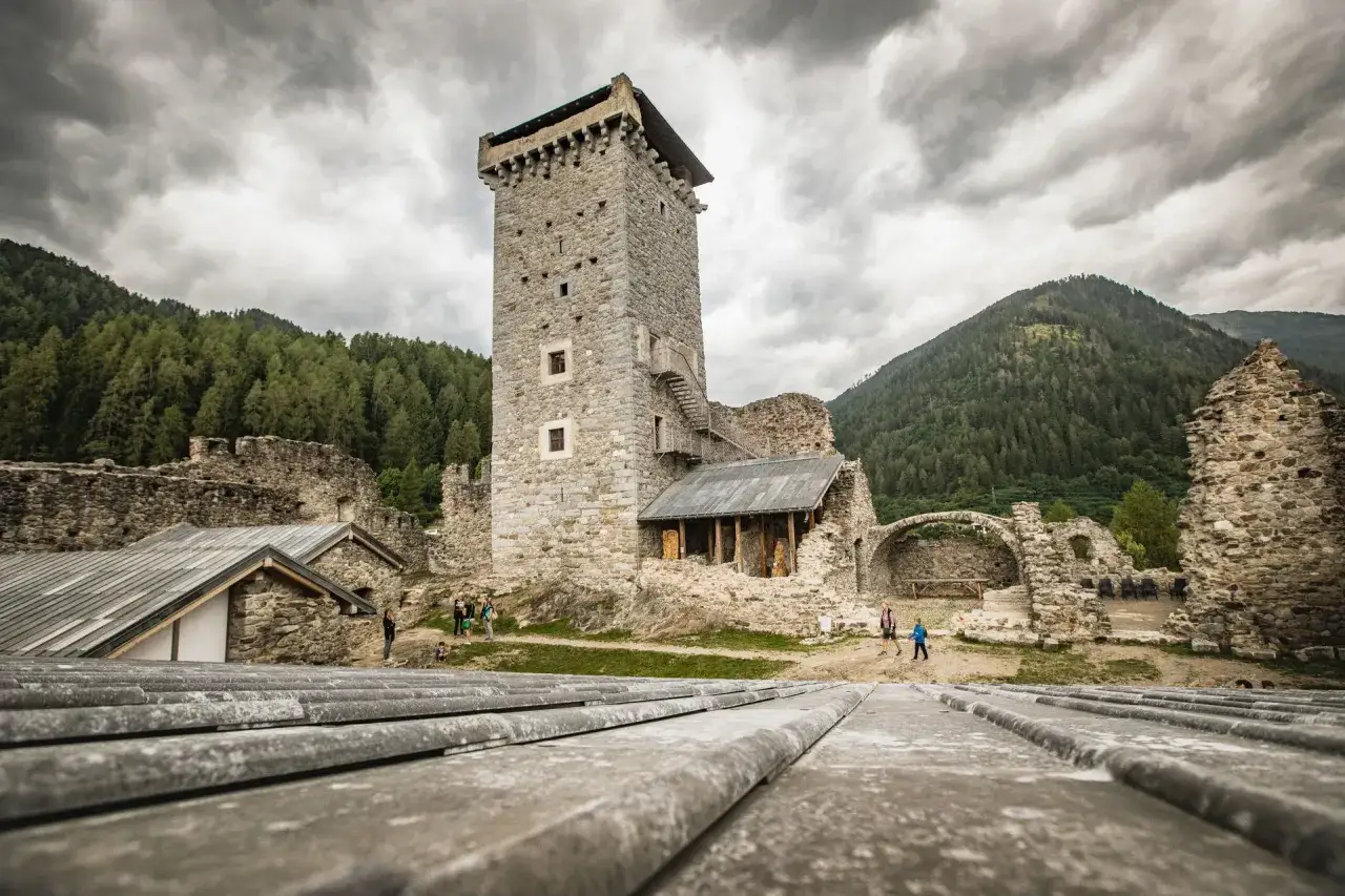Rovine del Castello di Ossana in Val di Sole, con la torre principale imponente e le montagne verdi sullo sfondo.