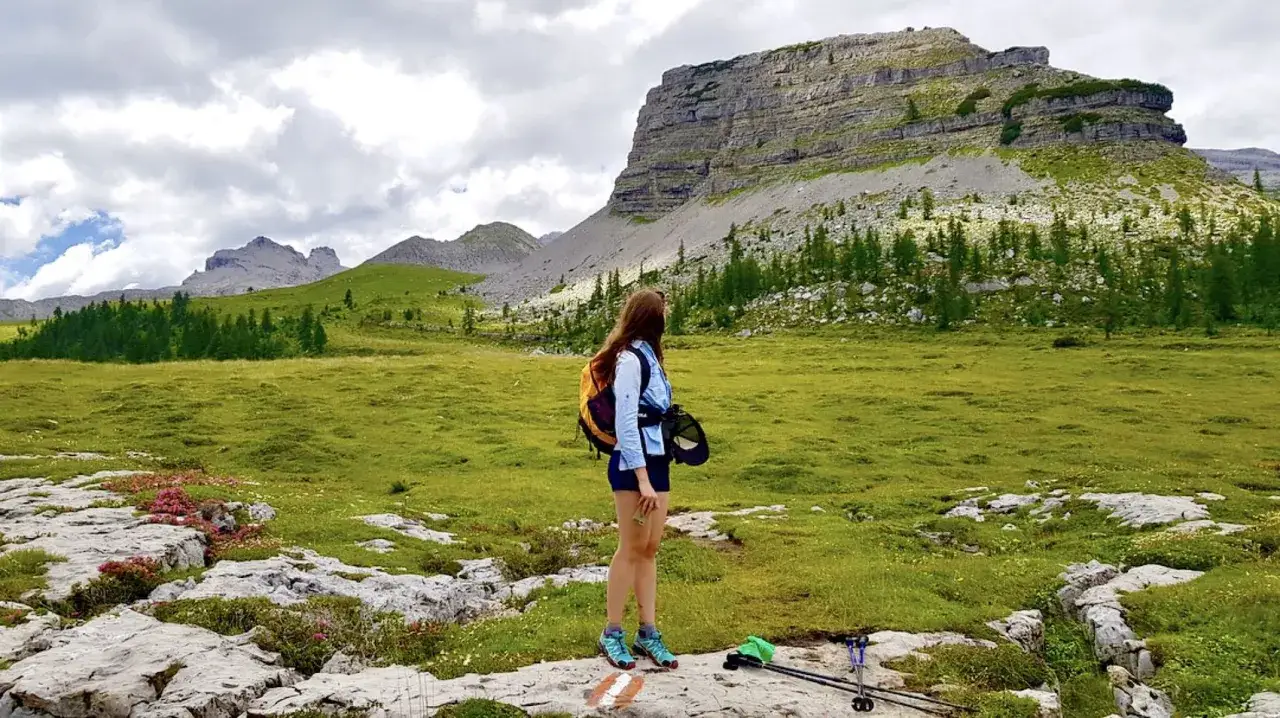 Ragazza con zaino ammira un paesaggio alpino con un imponente turrion basso e prati verdi.