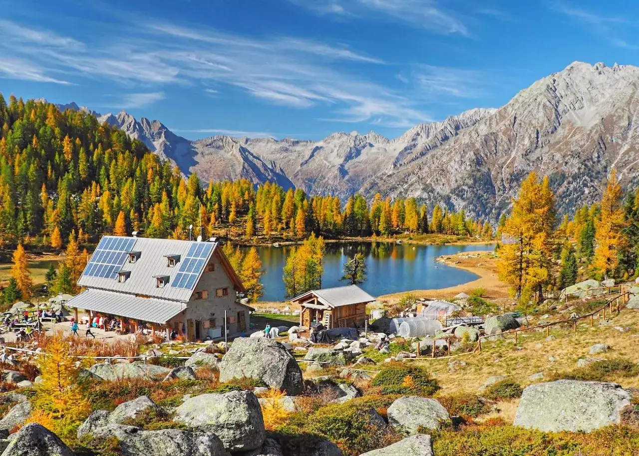 Rifugio alpino con pannelli solari ai laghi di San Giuliano, circondato da larici dorati e montagne maestose.