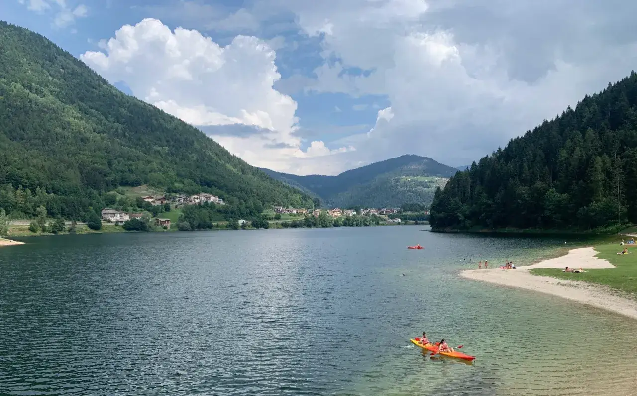 Lago di Serraia a Baselga di Pin&egrave;: cosa vedere? Un paesaggio incantevole con montagne verdi, un lago azzurro e persone che fanno kayak e prendono il sole.