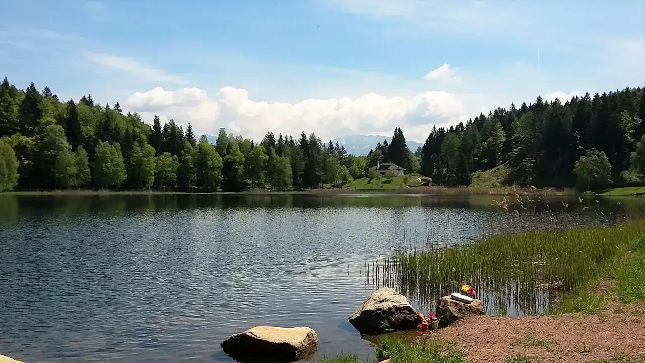 Tranquillo lago santo Val di Cembra, circondato da fitti boschi verdi e montagne sullo sfondo.