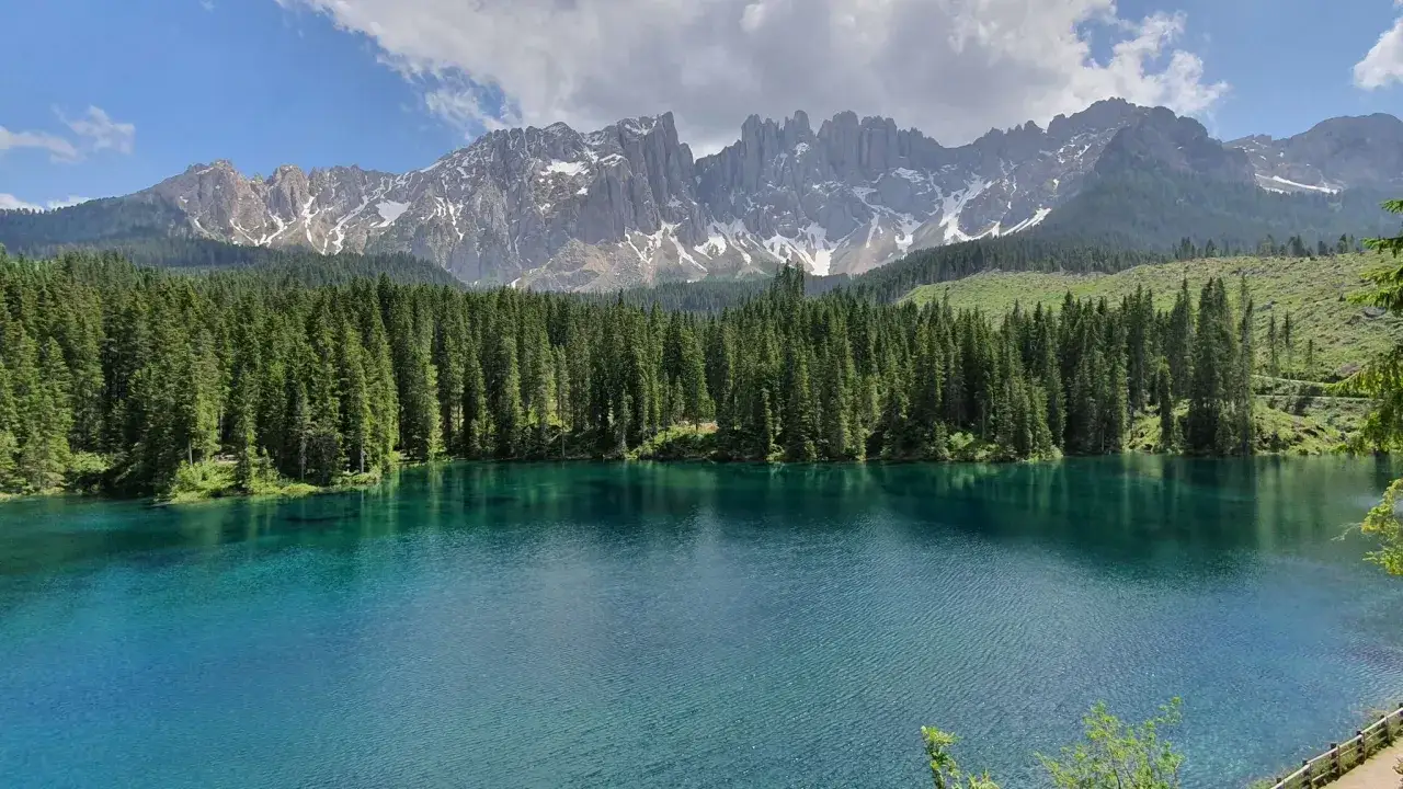 Laghi alpini in Val di Fassa, con acque cristalline che riflettono la foresta di conifere e le maestose vette dolomitiche innevate.
