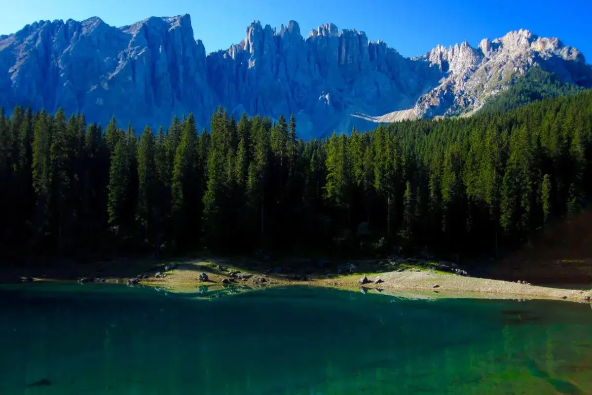 Lago alpino con acque smeraldine, circondato da fitti boschi di conifere e dominato dalle maestose cime delle Dolomiti.