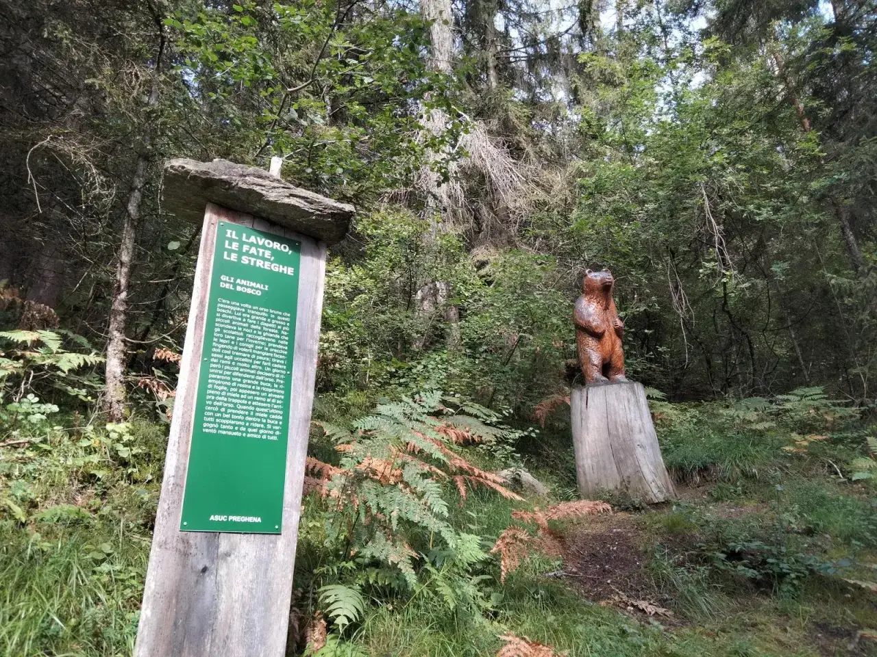 Segnaletica del sentiero delle fate nel bosco, con una scultura di orso su un ceppo.