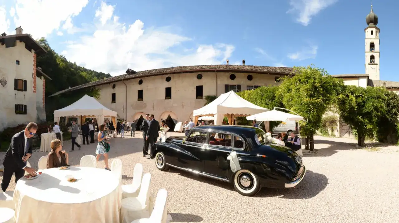 Matrimonio a Caldonazzo centro storico: auto d'epoca nera, tavoli allestiti, tende bianche e ospiti in attesa.