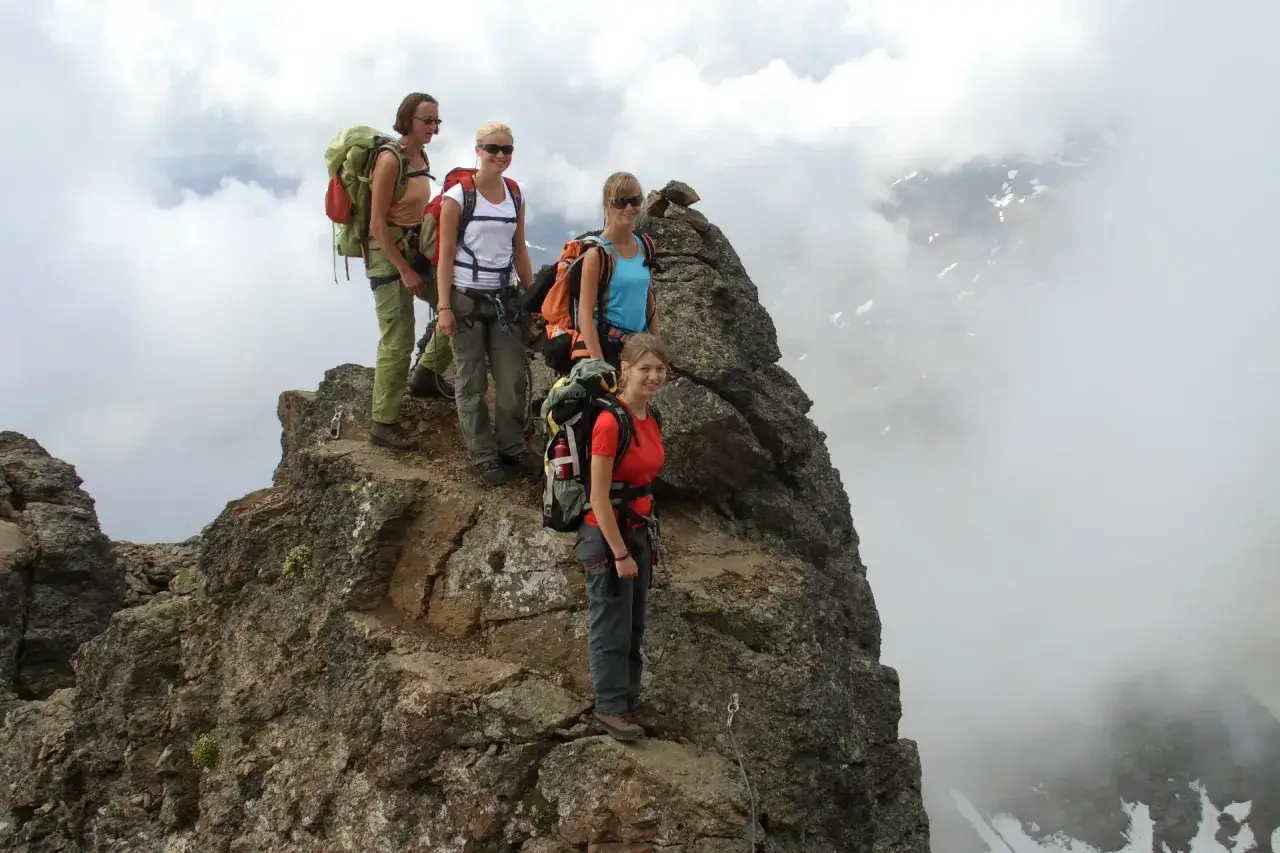Quattro escursionisti con zaini si fermano sulla cima Sternai, circondati da nuvole e nebbia, godendosi il panorama alpino.