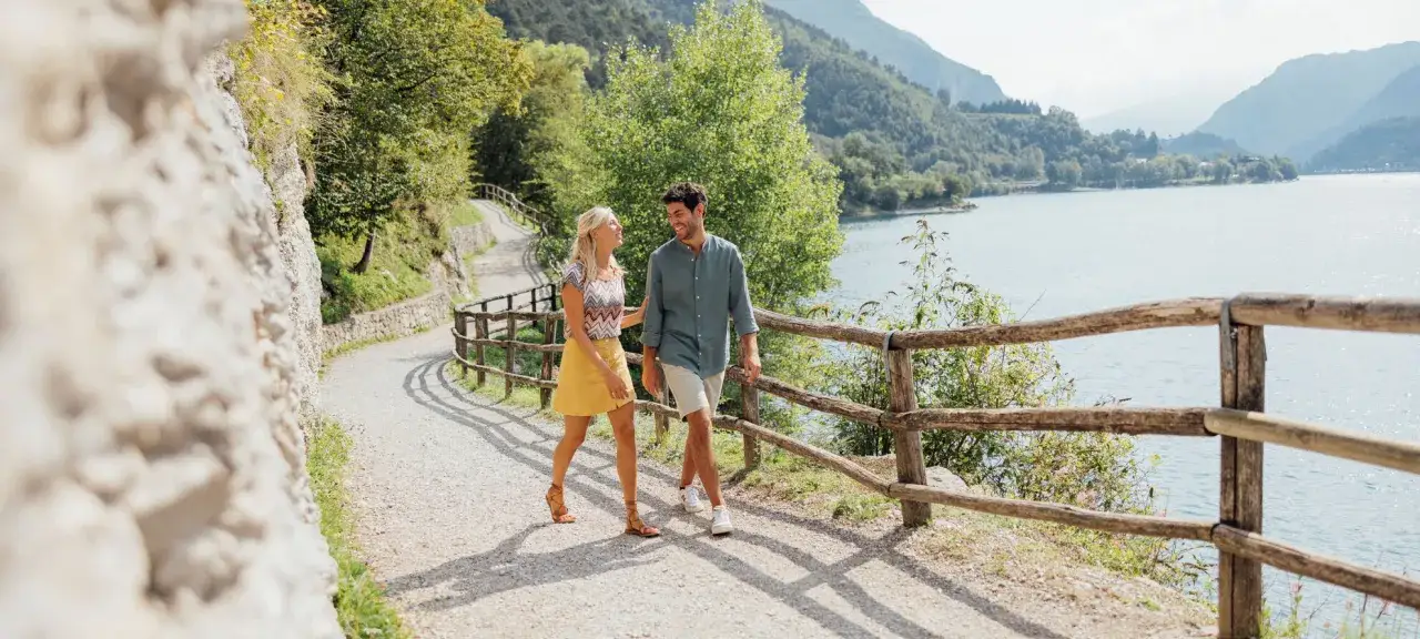 Coppia felice in passeggiate facili vicino a Trento, su un sentiero con vista lago e montagne.
