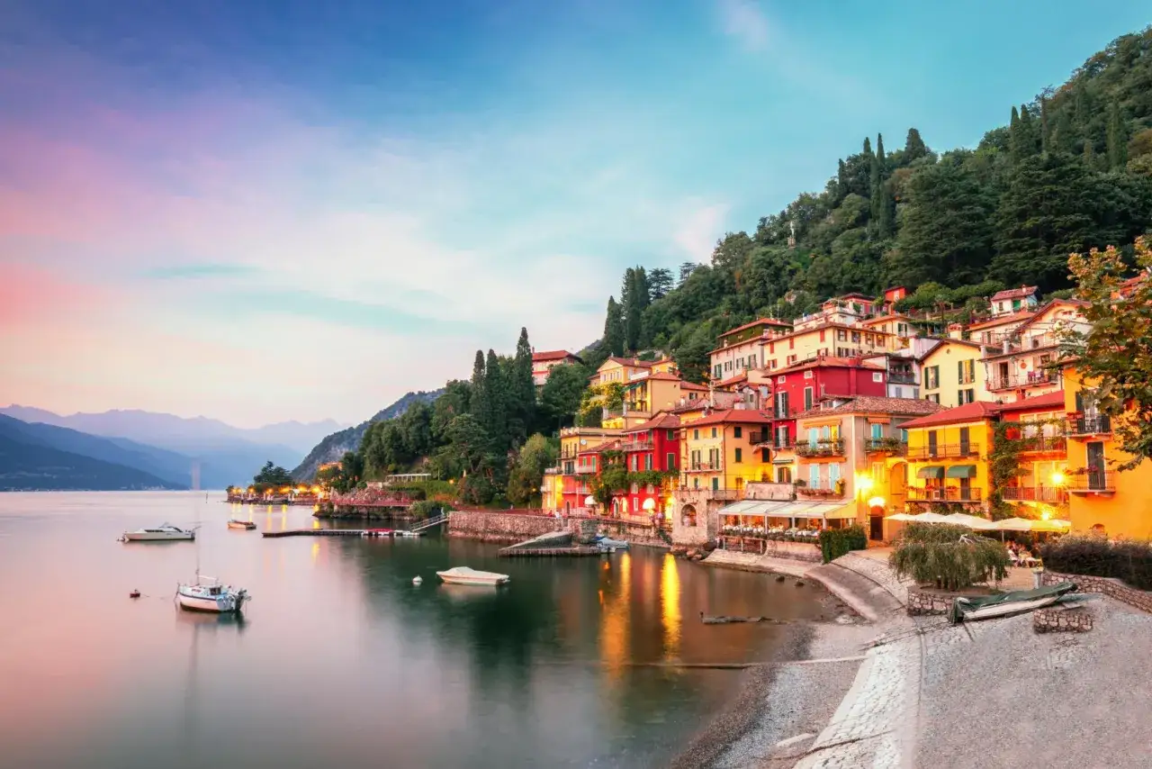 Colorate case aggrappate alla collina sul lago di Garda, con barche che galleggiano sull'acqua calma al tramonto. Un sogno per il giro del lago di Garda km.