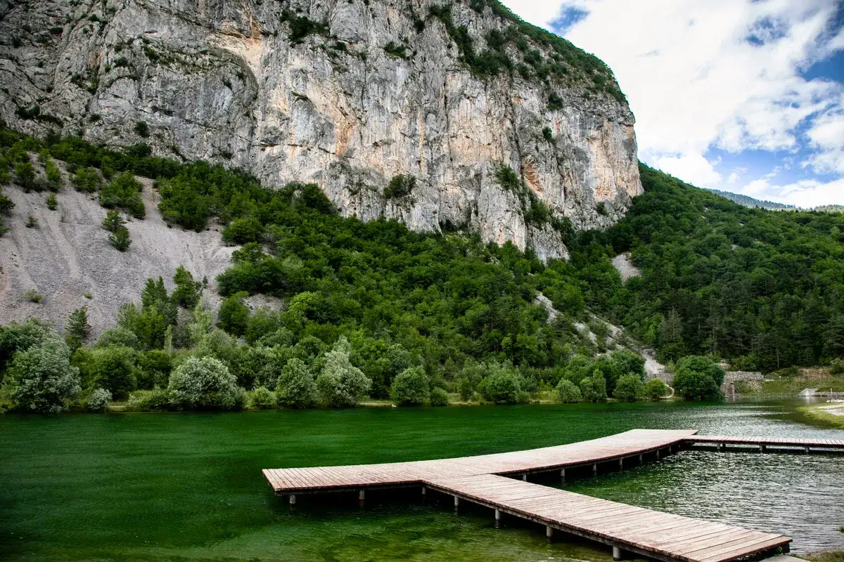 Molo in legno sul lago Nembia, circondato da rocce e vegetazione lussureggiante. Scopri come arrivare!