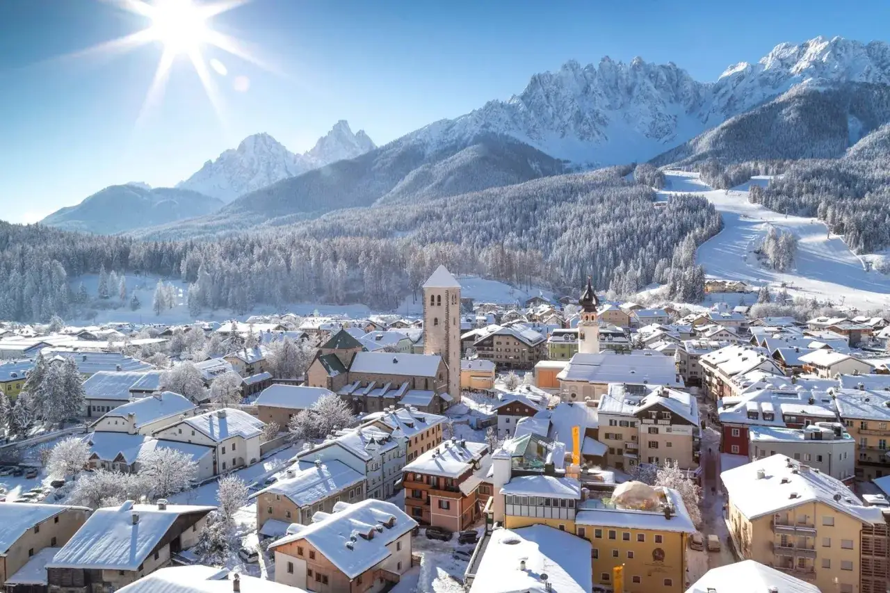 Un incantevole panorama di Trento inverno, con tetti innevati, montagne maestose e un sole splendente che illumina il borgo.