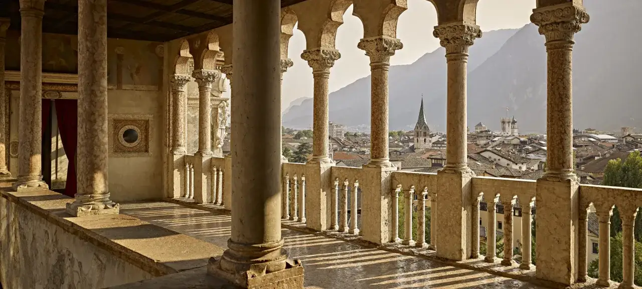 Loggiato con vista sulla città, un'atmosfera da museo trentino. Colonne classiche, archi e un panorama di tetti e montagne.