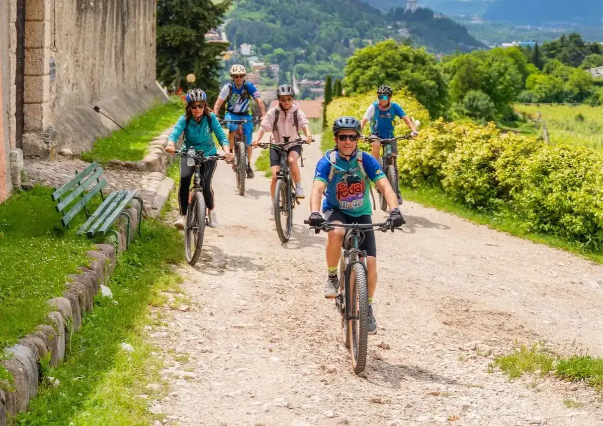 Ciclisti in gruppo su sentiero sterrato, godendosi gli eventi Trentino tra vigneti e montagne.