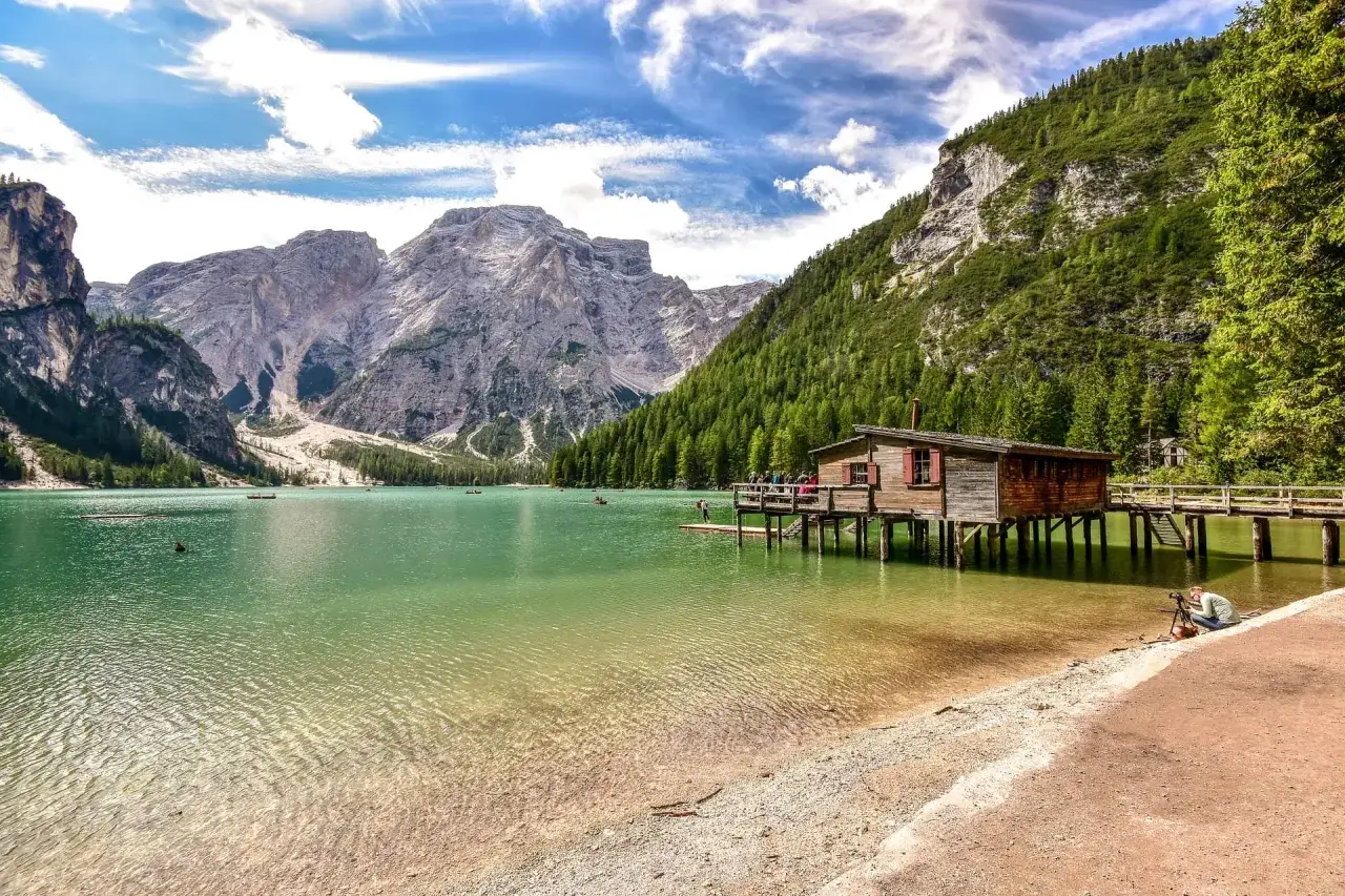 Il lago di Braies dove si trova &egrave; incastonato tra maestose montagne, con una baita di legno su palafitte e barche sull'acqua cristallina.
