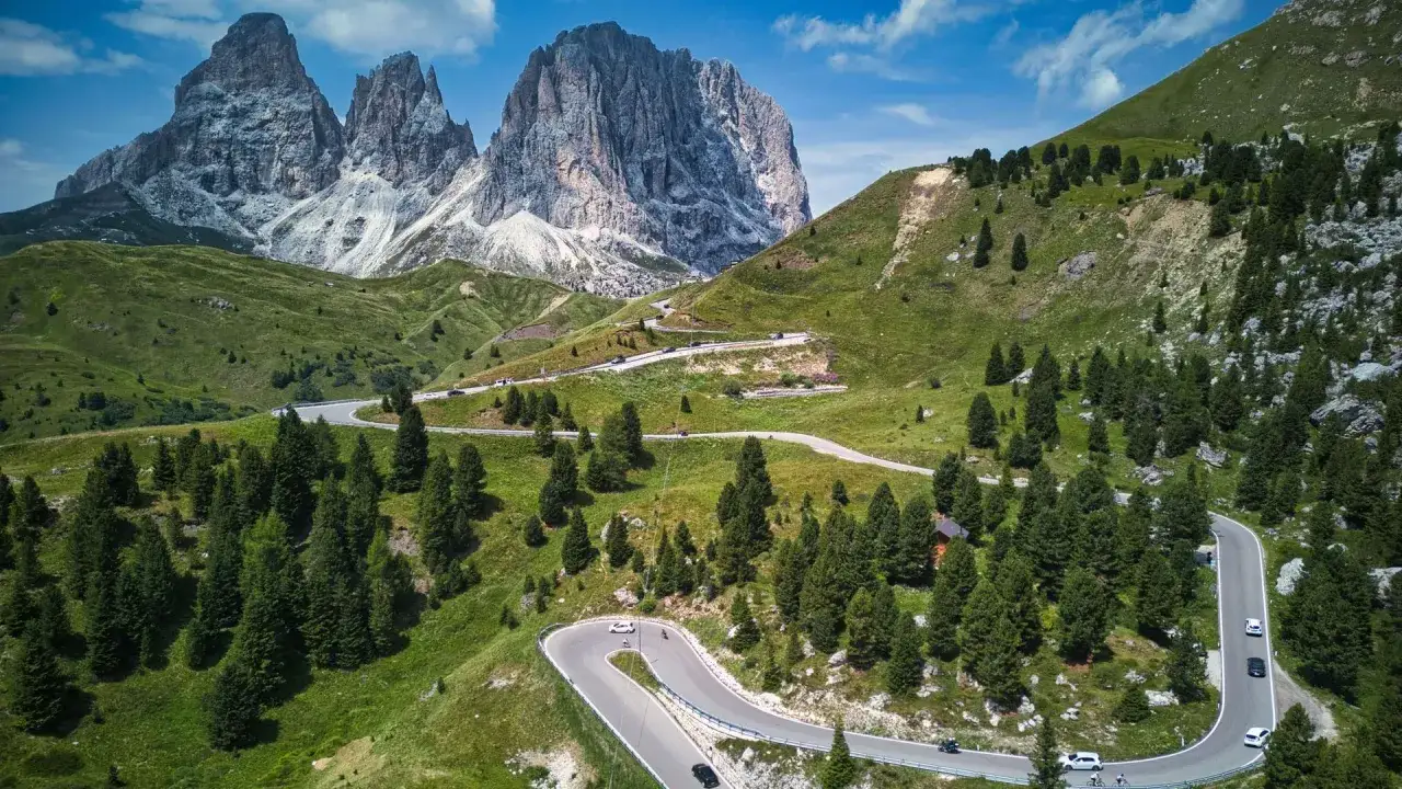Strada tortuosa verso il Sassolungo, con auto e moto che percorrono il passo Sella, un panorama mozzafiato vicino a Canazei.