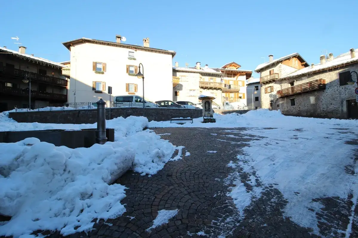 Piazza innevata a Miola di Pin&egrave;, con fontana e case tradizionali.