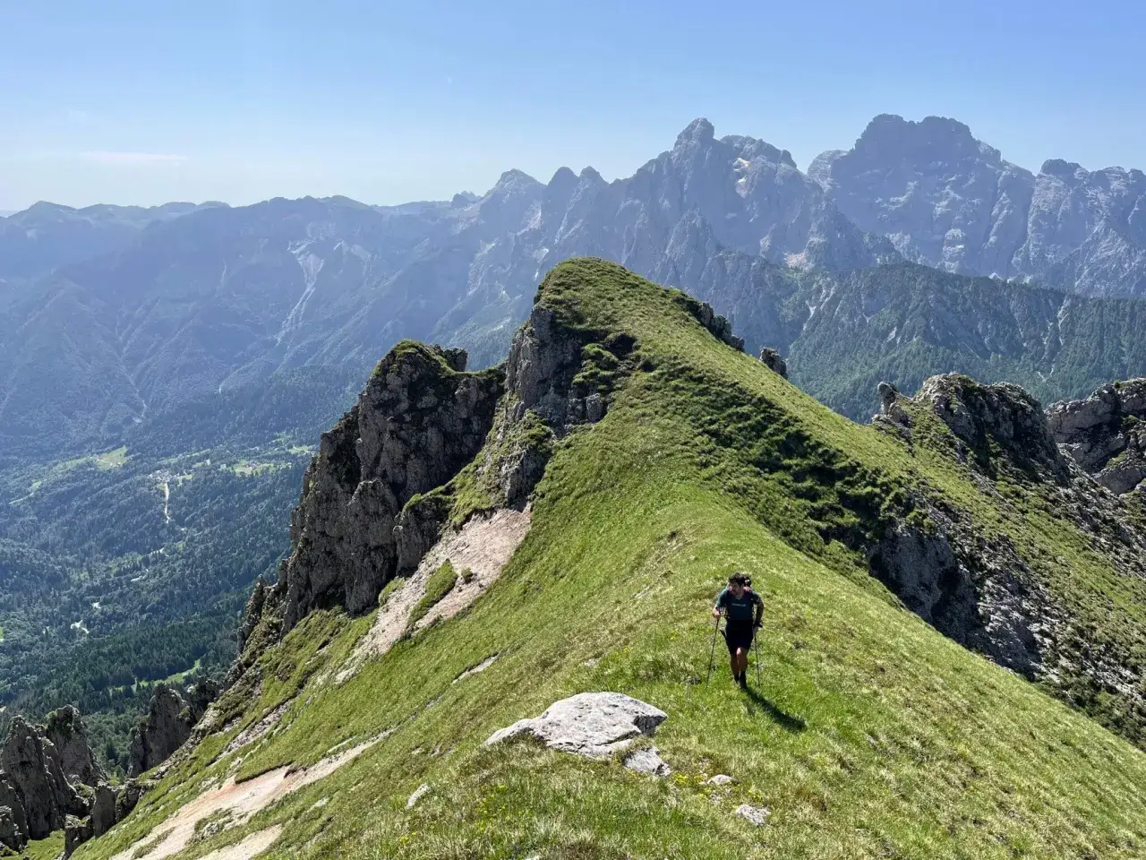 Escursionista su un crinale erboso, godendo della vista mozzafiato del passo Cereda in altitudine. Montagne maestose sullo sfondo.