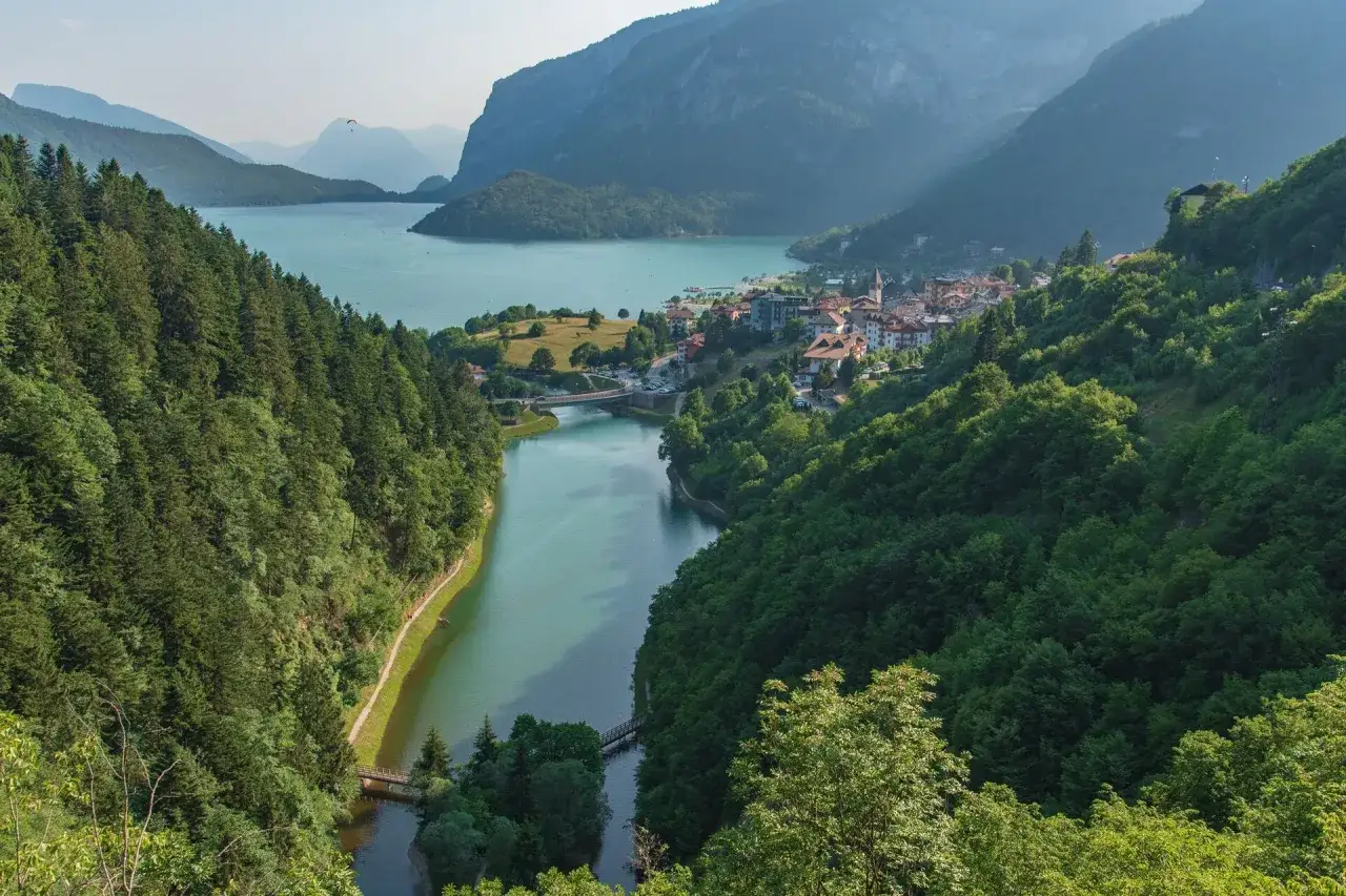 Vista panoramica di Molveno, con il lago turchese e le montagne sullo sfondo. Un parapendio vola nel cielo, un invito a scoprire cosa vedere a Molveno.