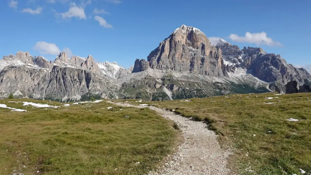 Sentiero ghiaioso tra prati verdi e cime innevate, ideale per un trekking pi&ugrave; giorni Dolomiti.