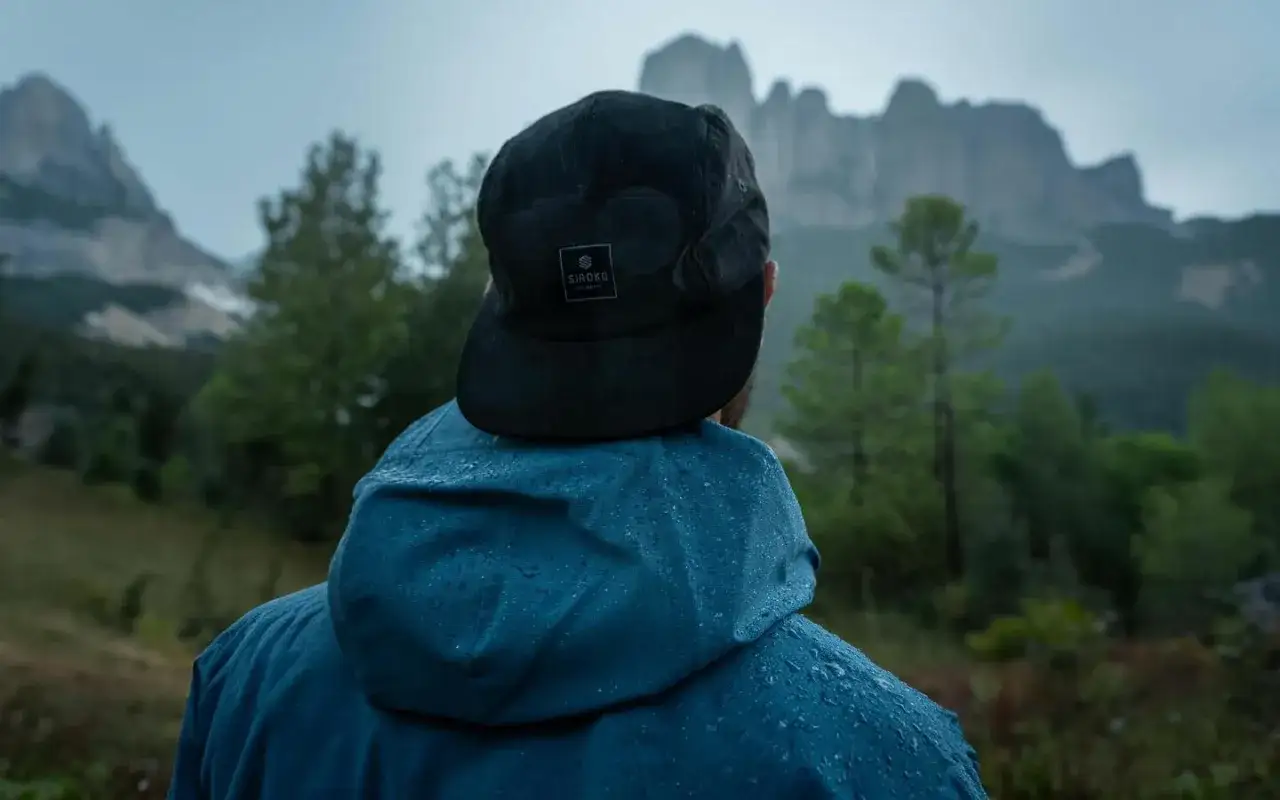 Uomo con cappellino nero e giacca blu impermeabile, pronto per affrontare il meteo in montagna a settembre.