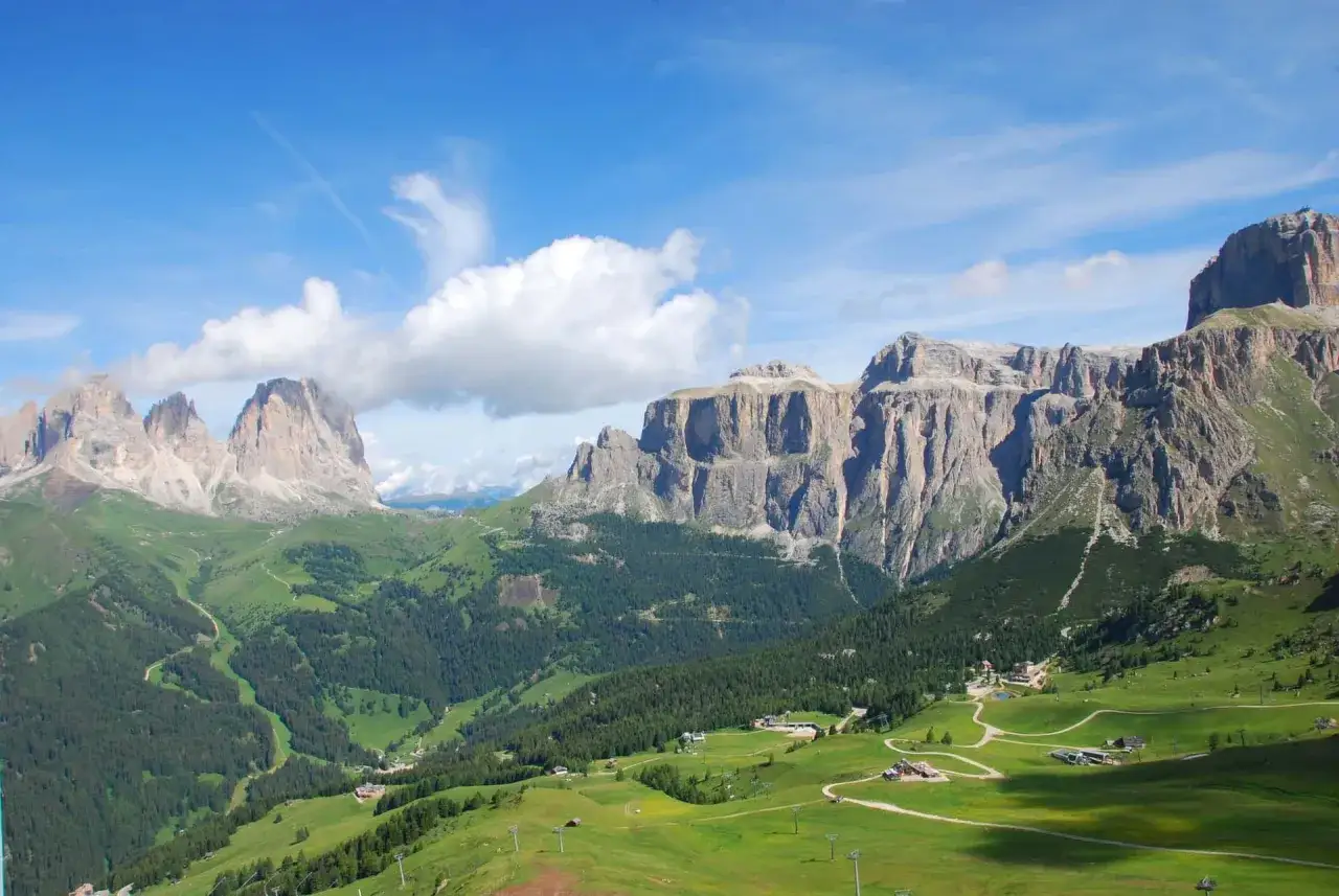 Panorami mozzafiato da Canazei al Passo Pordoi, con valli verdi, boschi e imponenti cime rocciose sotto un cielo azzurro.