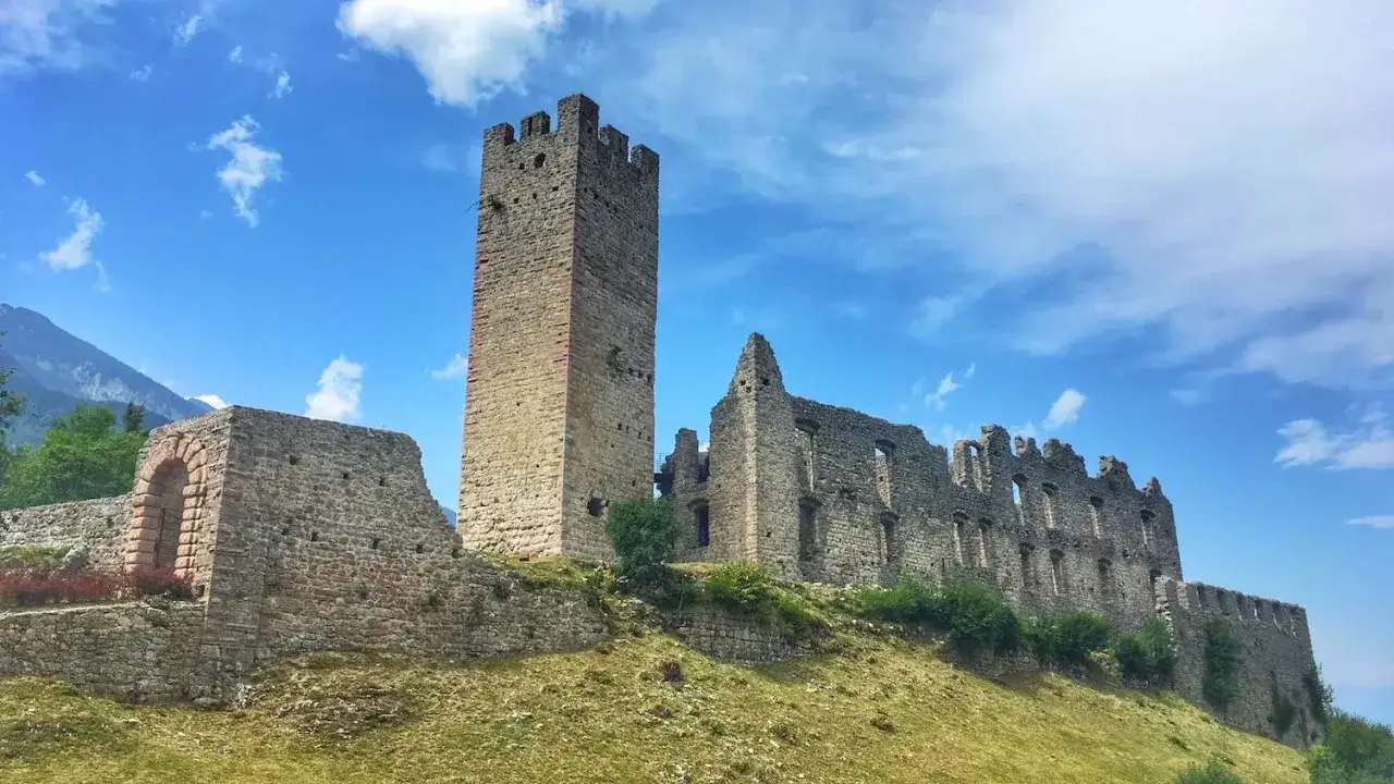 Rovine del castello di Altaguardia su una collina erbosa, con una torre imponente e mura di pietra sotto un cielo azzurro con nuvole bianche.