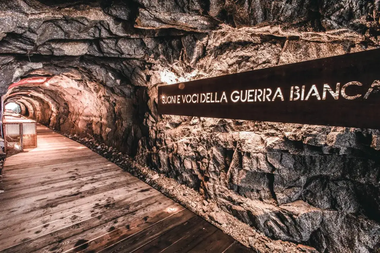 Un tunnel roccioso illuminato, con un cartello 