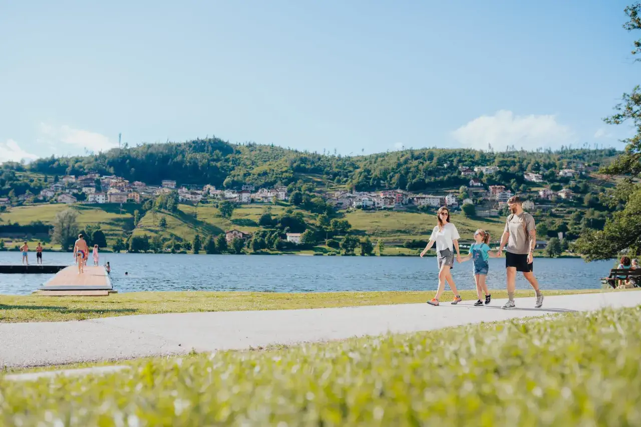 Famiglia passeggia sul lungolago di Serraia, con un villaggio sulle colline sullo sfondo.