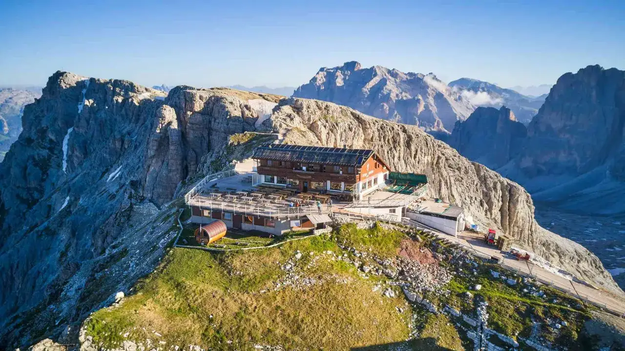 Rifugio alpino con terrazza panoramica, ideale per un trekking due giorni Dolomiti. Montagne imponenti sullo sfondo.