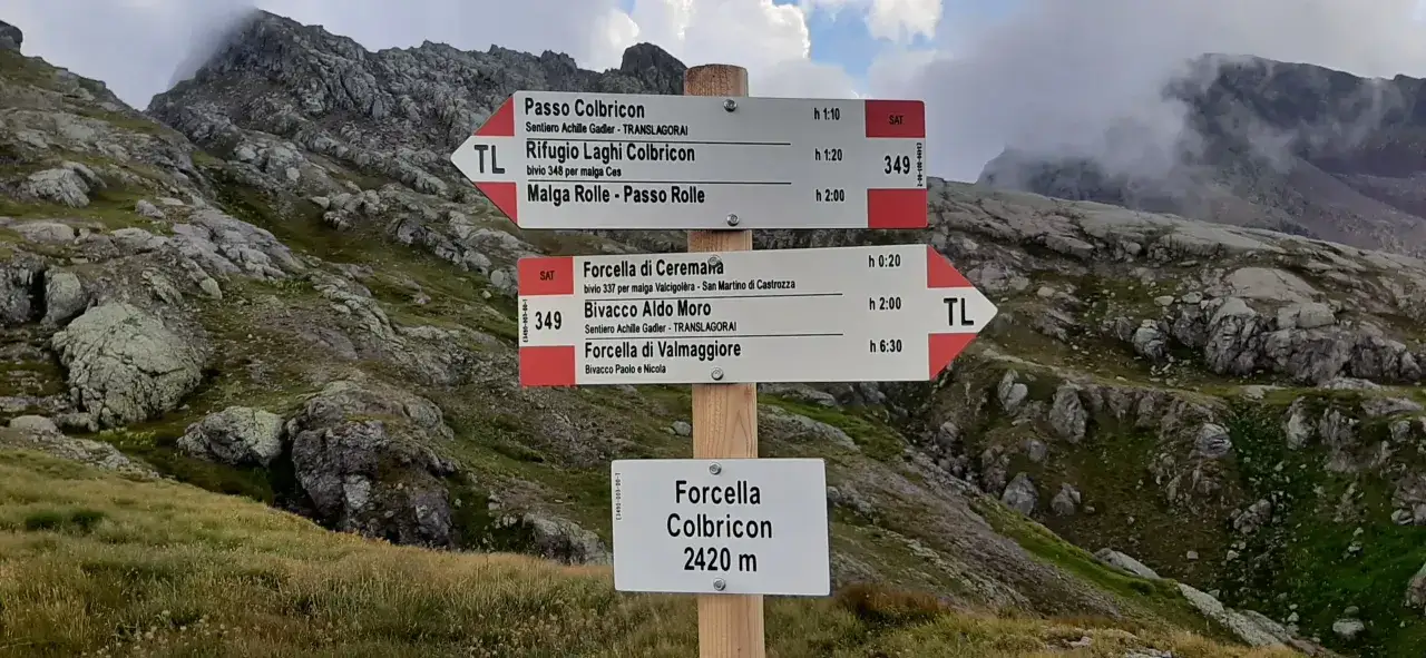Cartello segnaletico in montagna indica sentieri TRANSLAGORAI per Passo Colbricon, Rifugio Laghi Colbricon e Forcella di Valmaggiore.