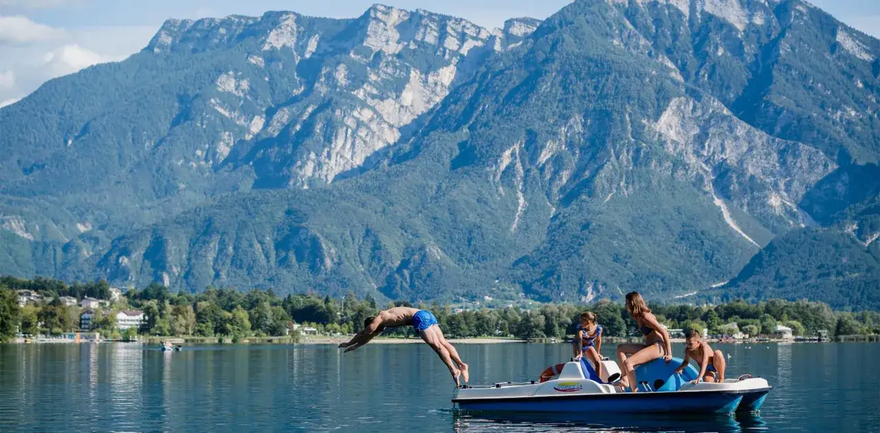 Un tuffo rinfrescante nel lago di Levico, con montagne maestose sullo sfondo e una famiglia che si gode la giornata in pedalò.