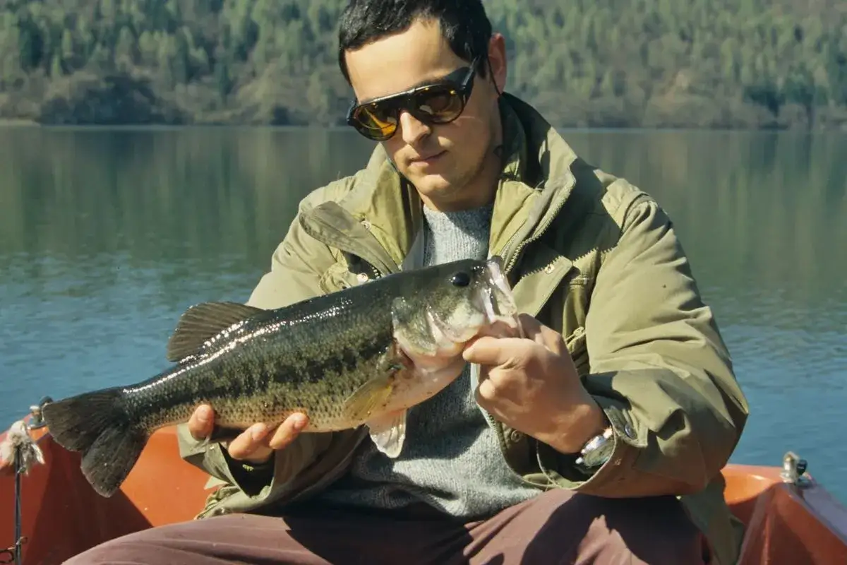 Uomo con occhiali da sole mostra un grosso pesce appena pescato sul Lago di Levico.