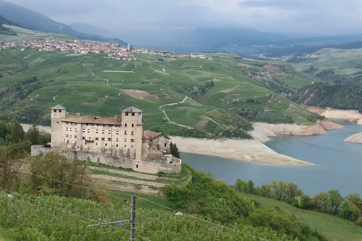 Castello di Thun domina il paesaggio del Val di Non, con vigneti a terrazze e un lago artificiale.