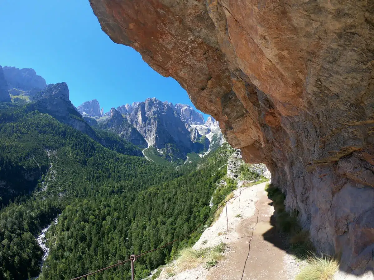 Sentieri panoramici vicino al Lago di Molveno, con un sentiero scavato nella roccia e una vista mozzafiato sulle montagne e una cascata.
