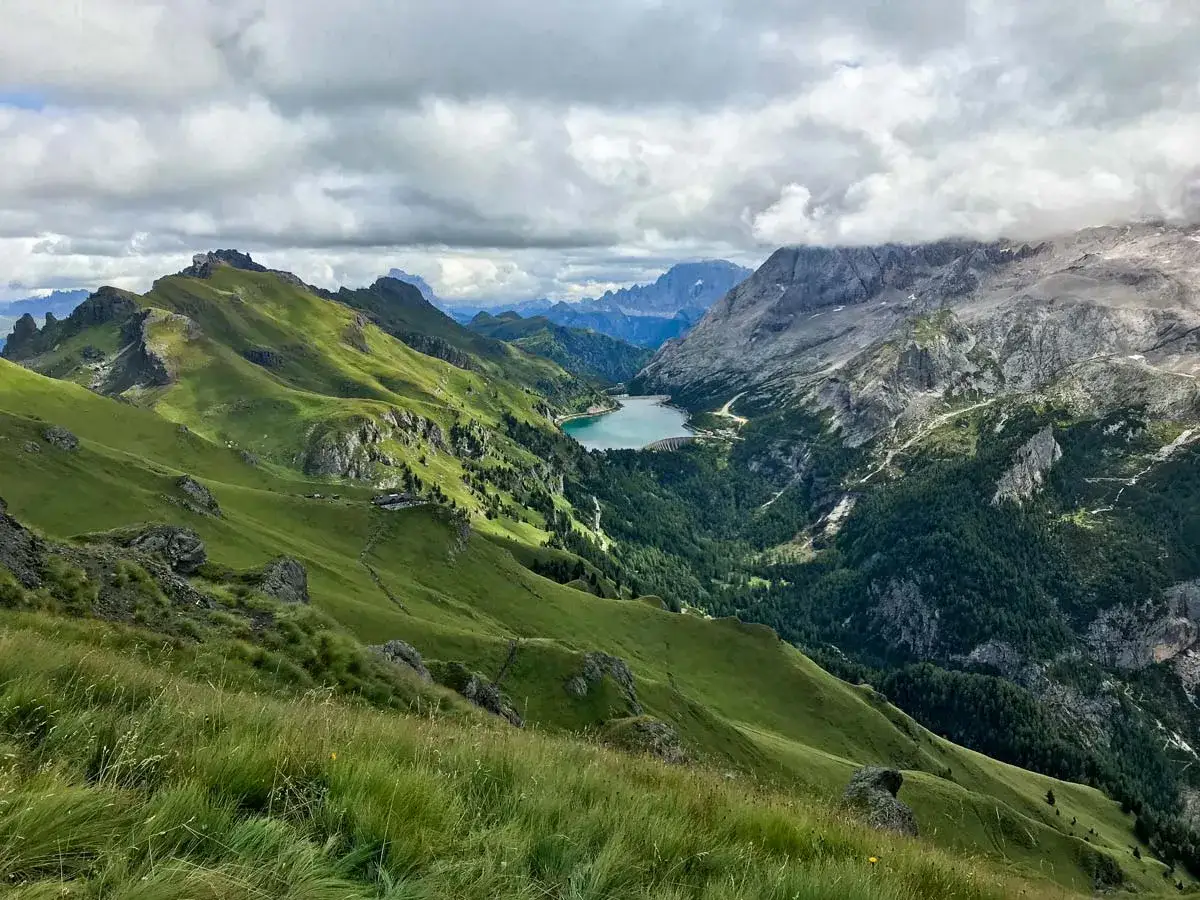 Viel del Pan: verdi pendii montani abbracciano un lago alpino, con cime rocciose e nuvole che incombono.
