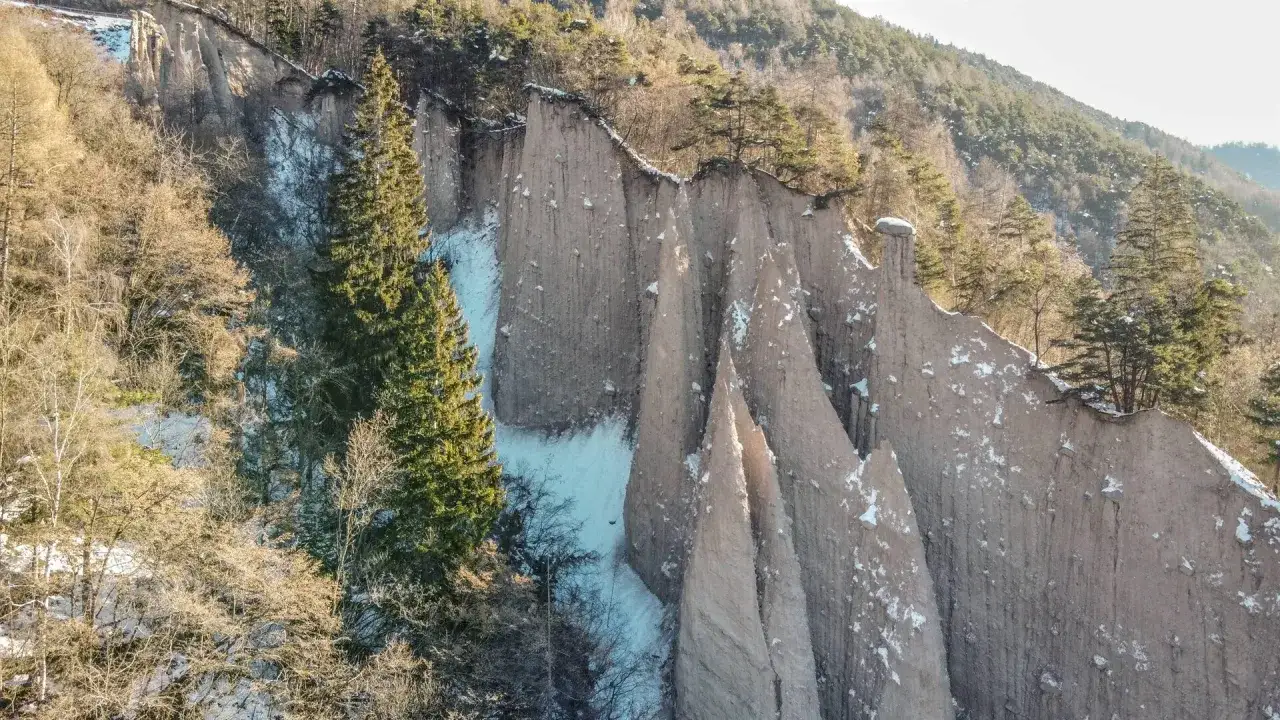 Le piramidi trentino, formazioni naturali uniche, si ergono maestose tra alberi spogli e neve, un paesaggio invernale suggestivo.