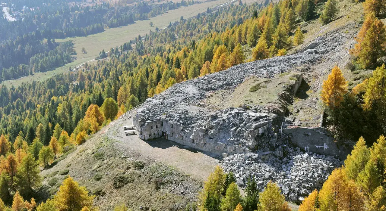 Antico forte zaccarana, parzialmente in rovina, incastonato tra i larici dorati autunnali su un pendio montano.