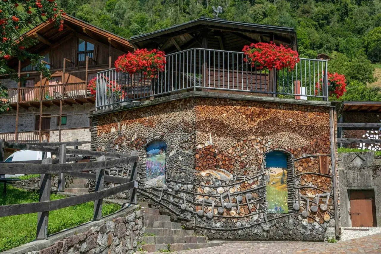 Un villaggio alpino con case in legno e pietra. Una facciata &egrave; interamente rivestita di legna da ardere, con dipinti che raffigurano paesaggi. Un vero spettacolo da vedere!