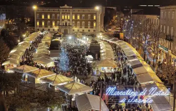 Un affollato Mercatino di Natale a Trento, con bancarelle illuminate, un albero scintillante e gente che passeggia tra le luci festive.