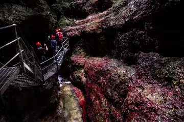 Esploratori con caschi rossi percorrono una passerella metallica nel **canyon Rio Sass fondo**, tra rocce scure e rosse.