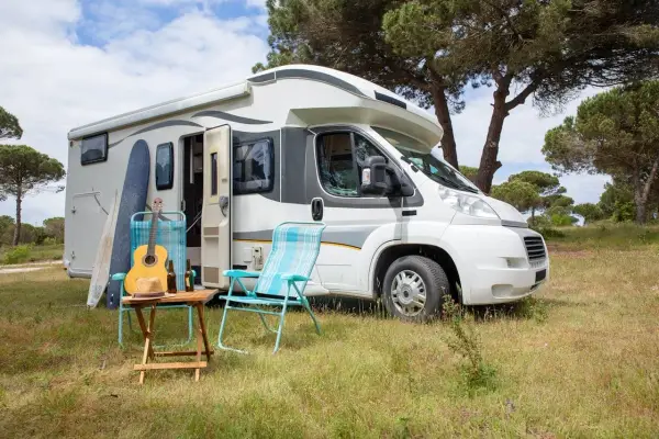 Un camper pronto per un tour in Trentino, con chitarra, cappello e sedie da campeggio in un prato verde.