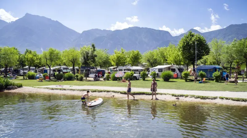 Giovani si godono il lago di Levico spiaggia, con campeggio e montagne sullo sfondo.