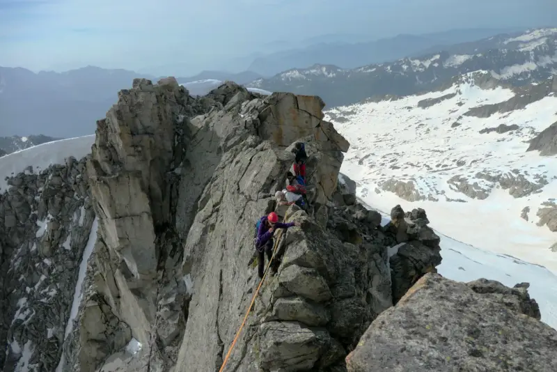 Alpinisti in cordata affrontano un crinale roccioso innevato, con la **cima Presanella** sullo sfondo.